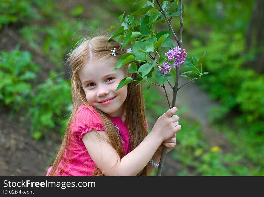 Smiling nice little girl holding lilacs at the trunk