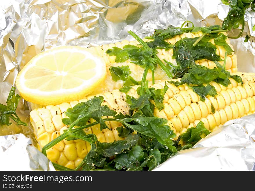 In aluminium foil steamed corn cobs decorated with parsley and lemon