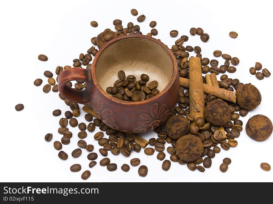 Coffee beans in cup and coffee beans and cinnamon sticks and chocolate truffles near cup on the white background