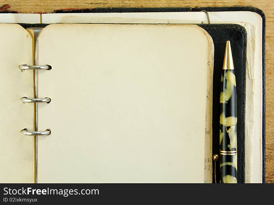 Close up corner of a vintage notebook and pen on a rustic wooden table.