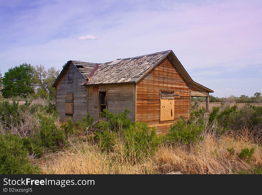 An old derelict wooden house with peeling tiles and broken and boarded windows in the semi-desert of Utah USA. An old derelict wooden house with peeling tiles and broken and boarded windows in the semi-desert of Utah USA.