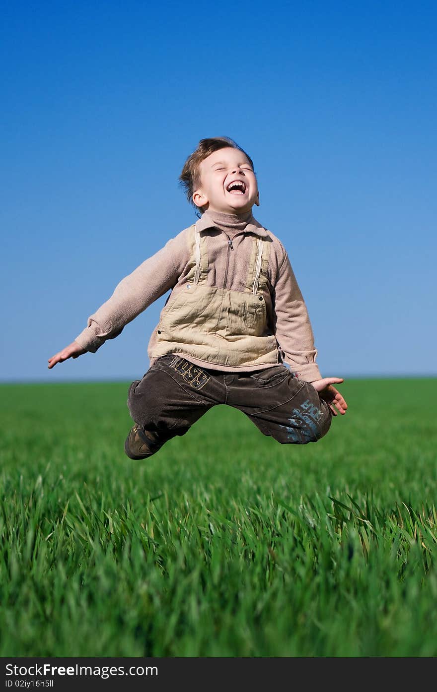 Happy little boy jumping in field against blue sky. Happy little boy jumping in field against blue sky