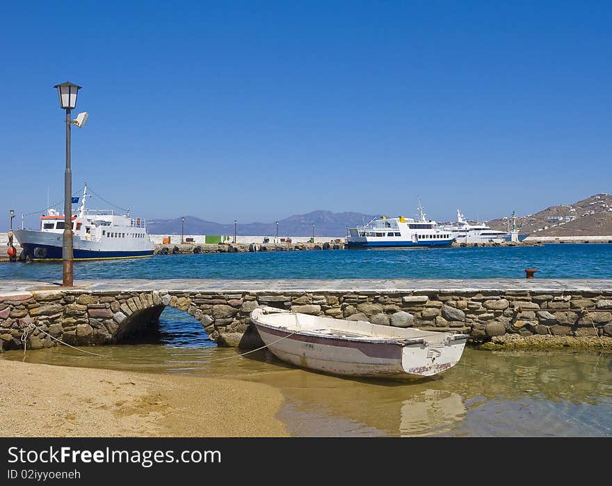 Lonely old fishing boat near the pier in the port of Mykonos on the background of parking pleasureboat