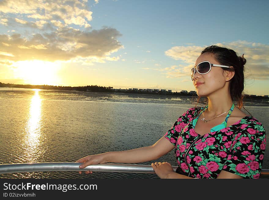 An Asian girl is appreciating the charming sunset on a yacht. An Asian girl is appreciating the charming sunset on a yacht.