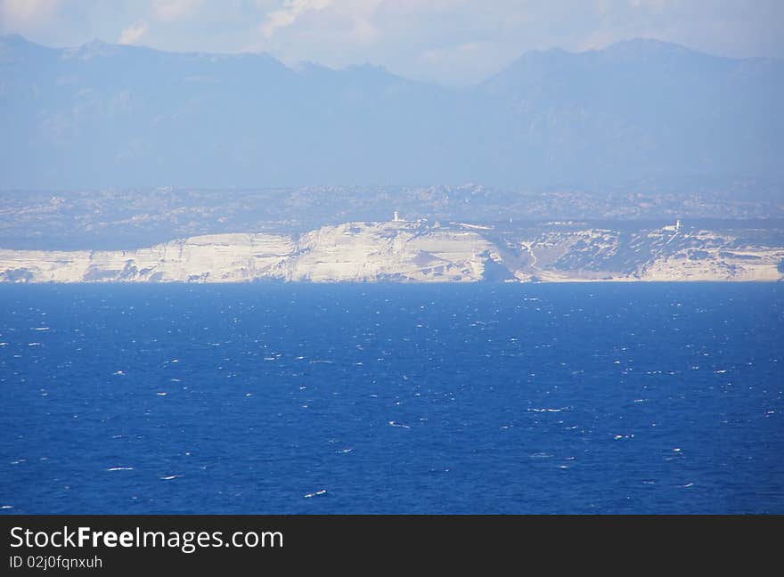 Straits of Bonifacio (Bocche di Bonifacio), strait between Sardinia (Italy) and Corsica (France) which divides the Tyrrhenian Sea from western Mediterranean Sea, and view of Bonifacio cliffs and mountains in the background. Straits of Bonifacio (Bocche di Bonifacio), strait between Sardinia (Italy) and Corsica (France) which divides the Tyrrhenian Sea from western Mediterranean Sea, and view of Bonifacio cliffs and mountains in the background