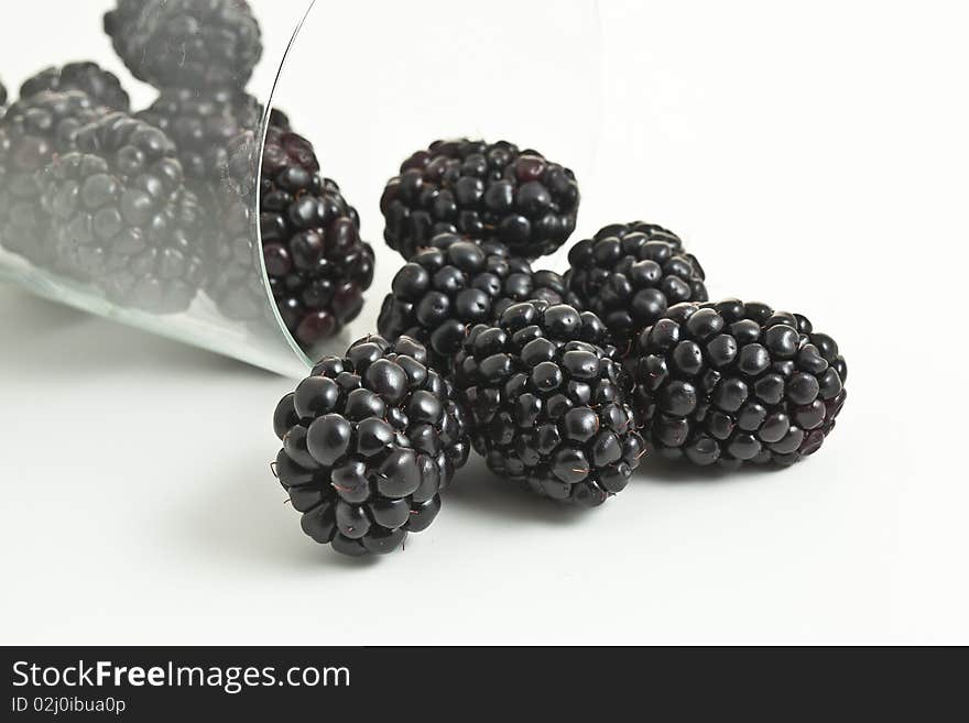 Blackberries in and out of a tipped on it's side glass with an isolated background. Blackberries in and out of a tipped on it's side glass with an isolated background