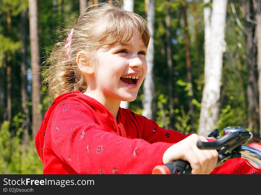 The joyful girl goes on a bicycle in the summer in park. The joyful girl goes on a bicycle in the summer in park