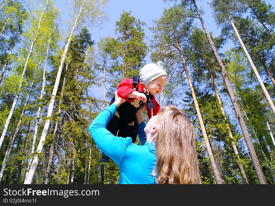 The girl lifts the kid up against trees in park in the summer. The girl lifts the kid up against trees in park in the summer