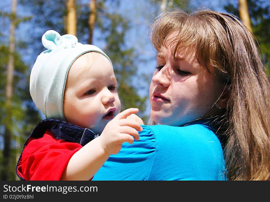 In the summer on the nature the girl in blue clothes holds on hands of the small child of the boy and looks at it. In the summer on the nature the girl in blue clothes holds on hands of the small child of the boy and looks at it