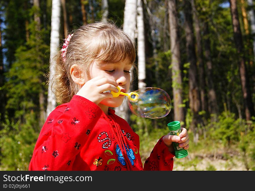 In the summer in park the girl in red clothes inflates a soap bubble. In the summer in park the girl in red clothes inflates a soap bubble