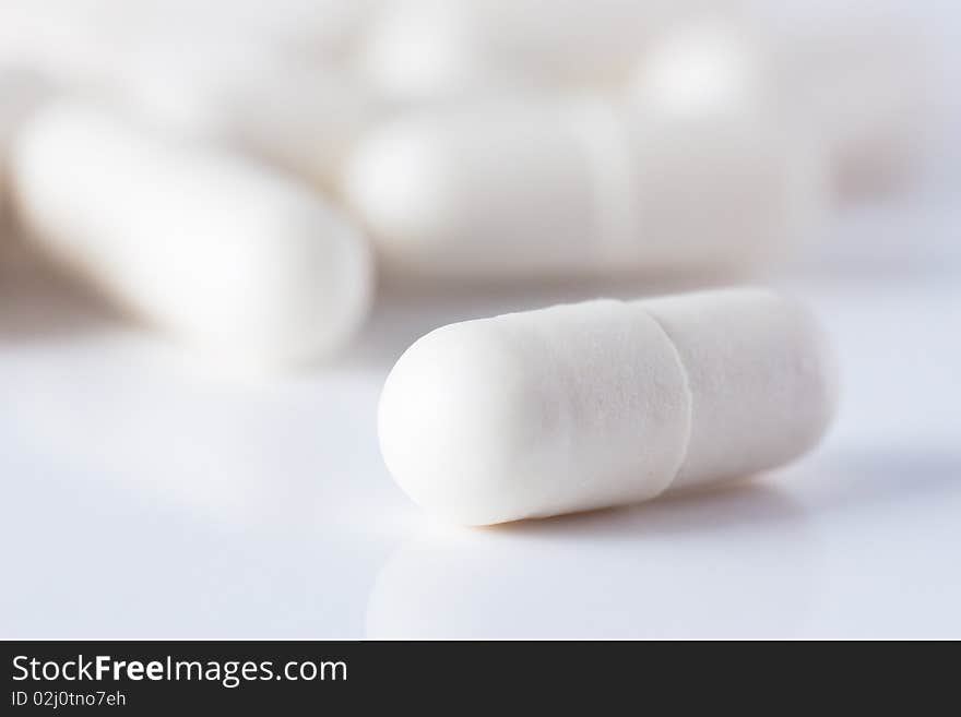 Macro shot of white capsuled pill and a heap of same pills defocused on background