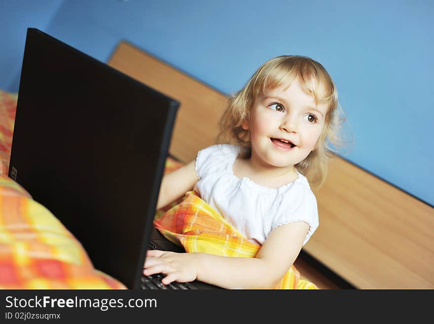 Cheerful little girl with laptop sits on bed of parents