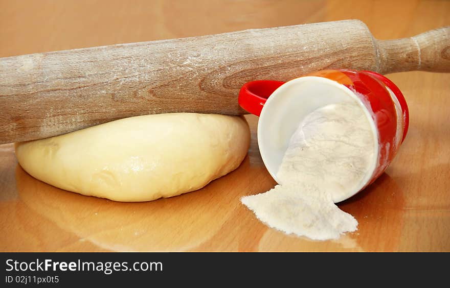 Rolling pin over dough and cup with flour on table in kitchen