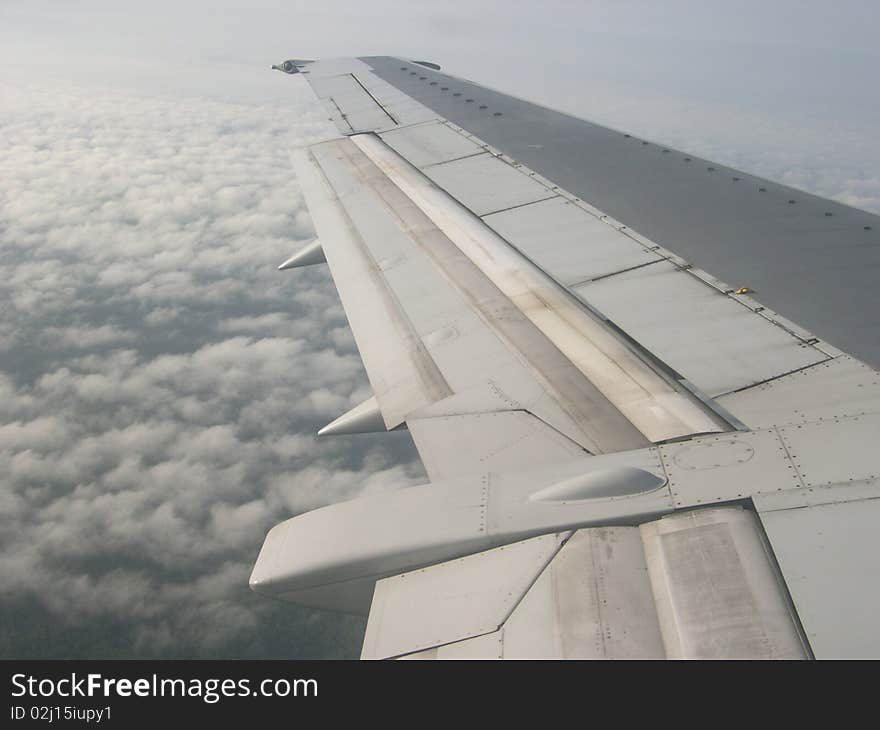 The wing of an airplane as seen from the aircraft window with the soft fluffy clouds as background. The wing of an airplane as seen from the aircraft window with the soft fluffy clouds as background.