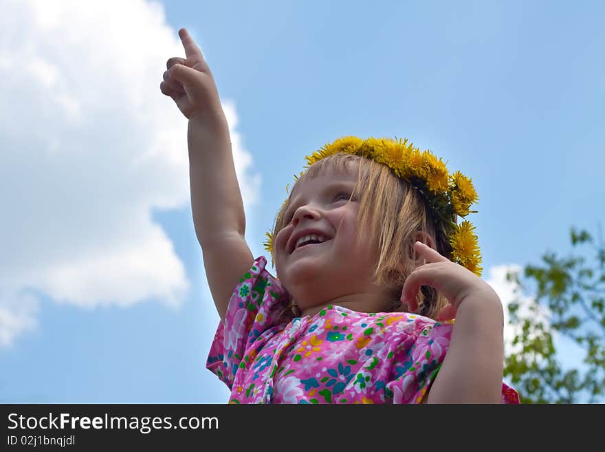 Portrait of little girl in dandelion crown pointing upwards