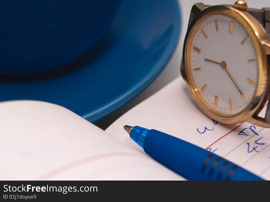 The open notebook, pen, watch and a cup close up. The open notebook, pen, watch and a cup close up