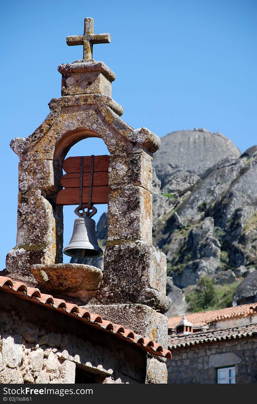 Old stone bell tower with cross on sky and rocks background (Portugal)