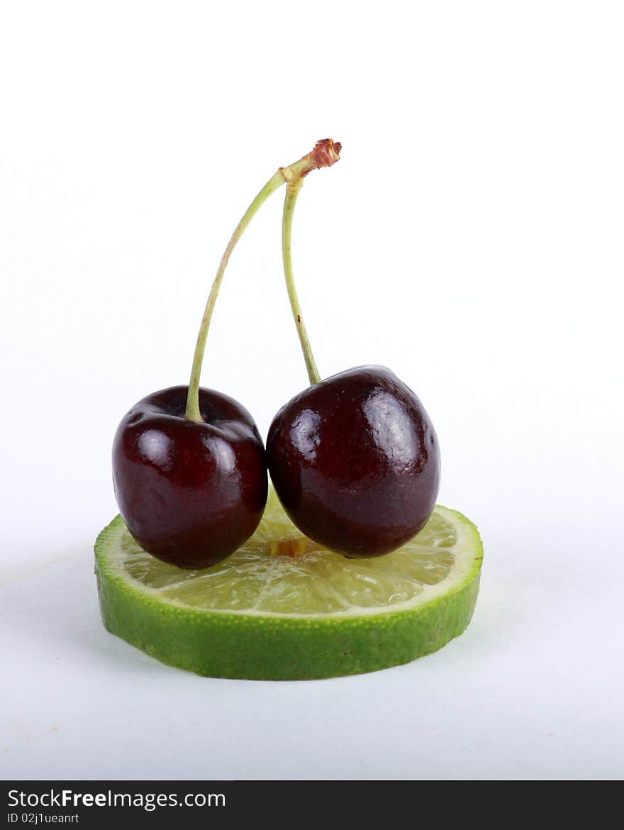 Cherries resting atop lime slice isolated. Cherries resting atop lime slice isolated