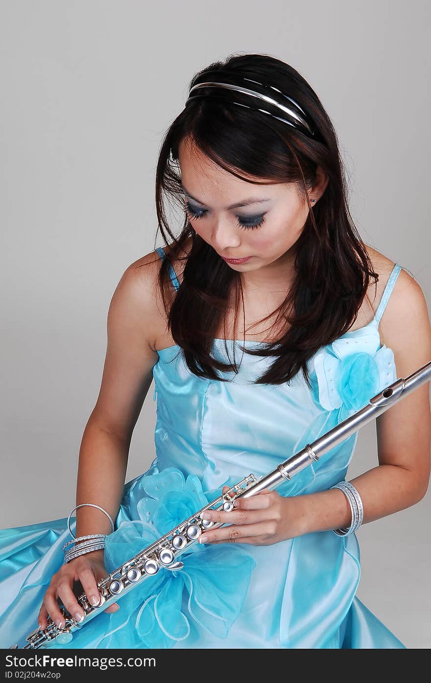 A young Asian woman in an light blue evening dress holding the flute standing in the studio for light gray background. A young Asian woman in an light blue evening dress holding the flute standing in the studio for light gray background.