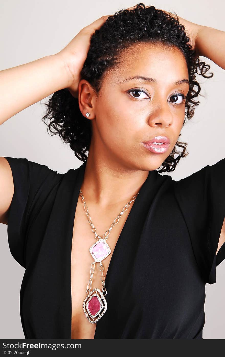 A beautiful Hispanic woman standing in the studio for a portrait with her black curly hair, in a black dress and nice necklace, light gray background. A beautiful Hispanic woman standing in the studio for a portrait with her black curly hair, in a black dress and nice necklace, light gray background.