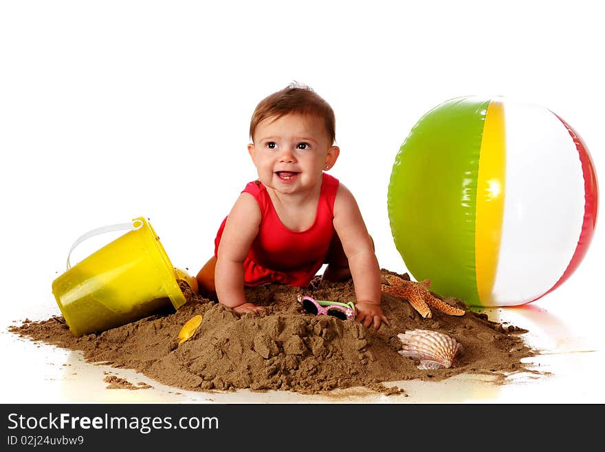 A happy baby girl crawling over a sand pile with beach toys, sunglasses and seashells nearby. A happy baby girl crawling over a sand pile with beach toys, sunglasses and seashells nearby.