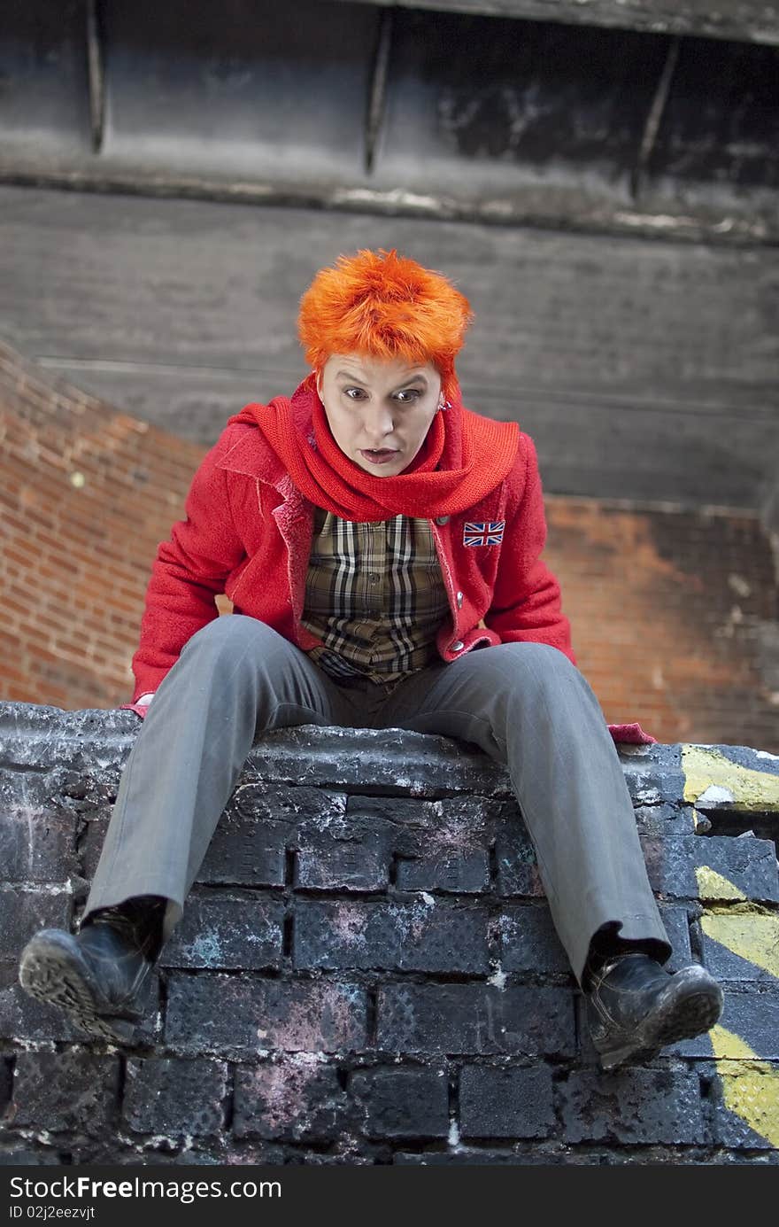 Red-haired woman is sitting on the edge of the wall and looks very surprised. Red-haired woman is sitting on the edge of the wall and looks very surprised