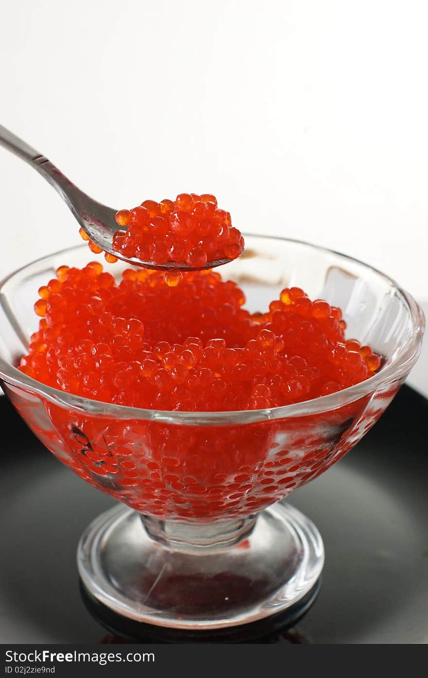 Red caviar in a glass vase on a black plate