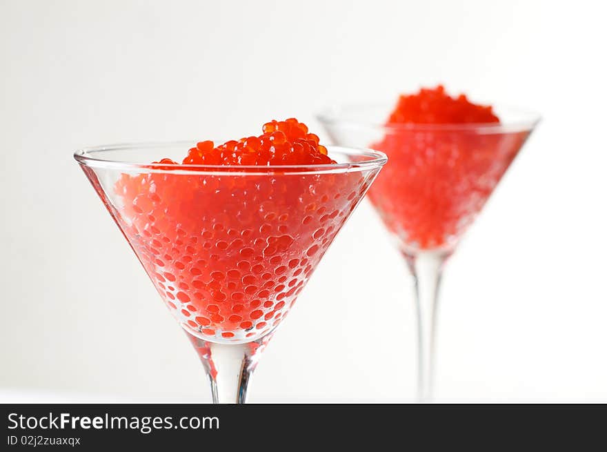 Two servings of red caviar in glass goblets on a white background