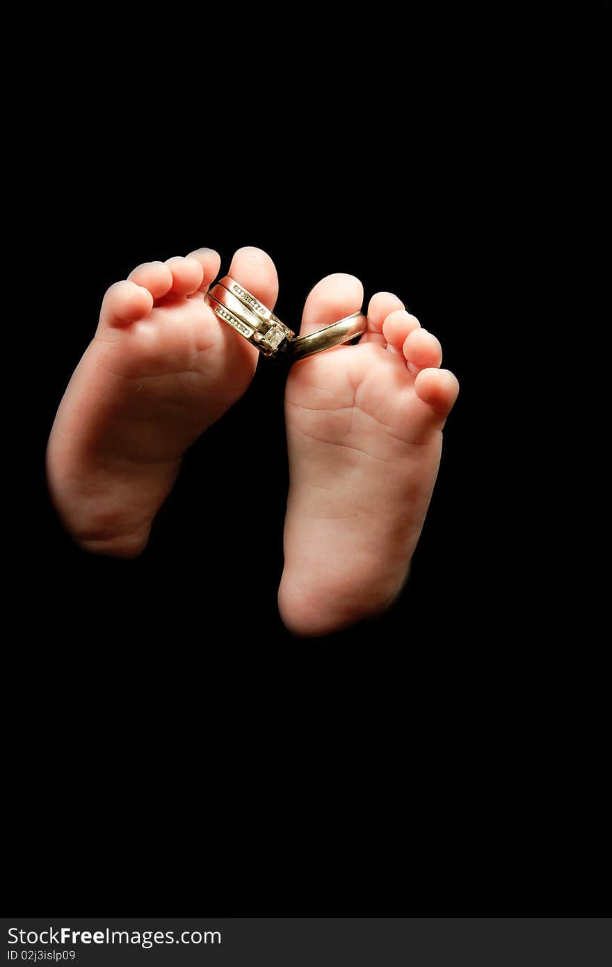 A baby's feet with wedding bands on toes - isolated on black. A baby's feet with wedding bands on toes - isolated on black