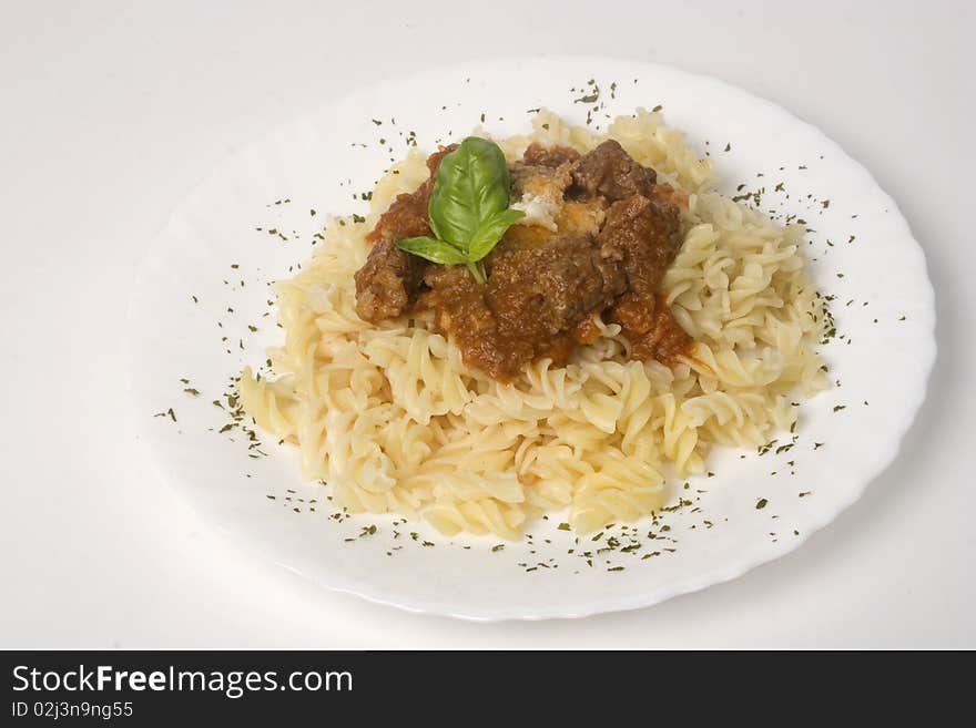 Fusilli with meat ragout, goulash, stewed beef on plate. Basil leaf and sheese on top. Isolated on white background.