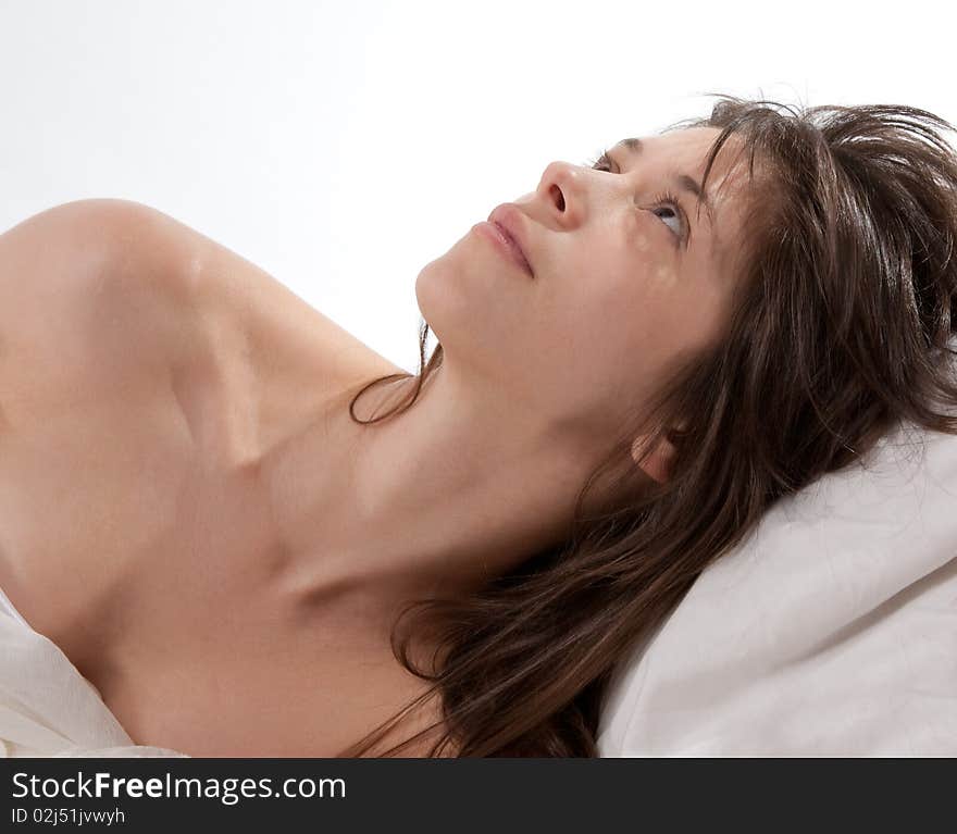 A portrait of a young woman on a white pillow looking up thoughtfully. A portrait of a young woman on a white pillow looking up thoughtfully