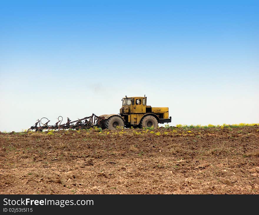 Working yellow tractor, ploughing the field. Working yellow tractor, ploughing the field