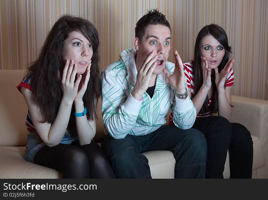 Three friends sitting on the couch in the living room and watching something scary on TV