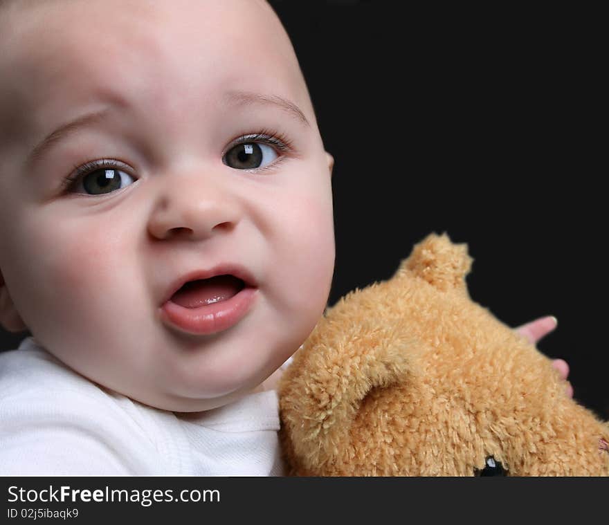 Baby boy against a dark background holding his bear