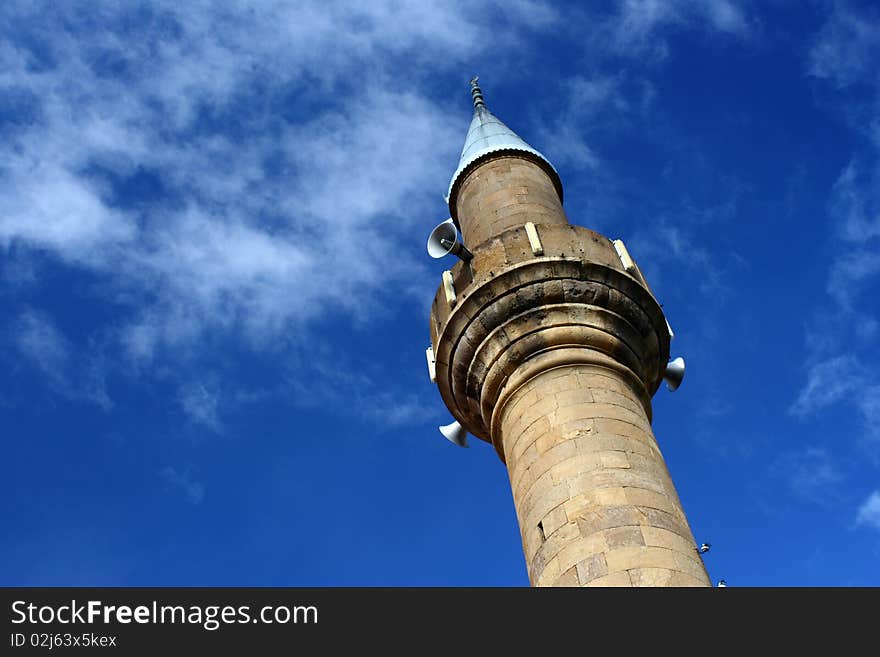 The minaret of a Turkish mosque shot at an angle against the blue sky. The minaret of a Turkish mosque shot at an angle against the blue sky