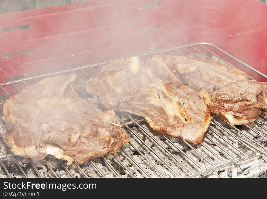 Some slices of beef on the grill with smoke. Some slices of beef on the grill with smoke