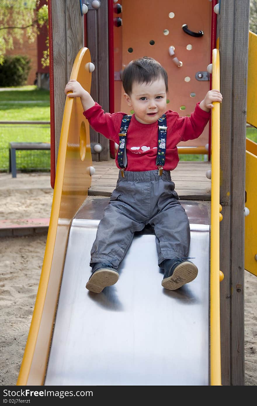 A little boy on slide in an outdoors playground. A little boy on slide in an outdoors playground.