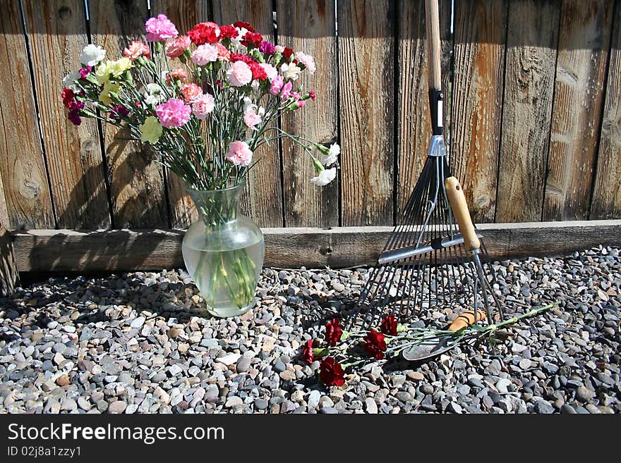 Garden tools on gravel with red carnations and garden wooden fence. Garden tools on gravel with red carnations and garden wooden fence