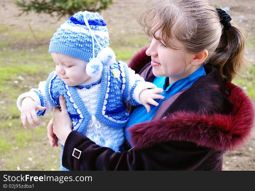 The small child in a white-blue knitted suit at the woman on hands in the spring on walk. The small child in a white-blue knitted suit at the woman on hands in the spring on walk