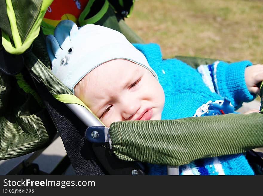 In the summer the small ten-monthly child in a blue suit sits in a green carriage the dissatisfied. In the summer the small ten-monthly child in a blue suit sits in a green carriage the dissatisfied