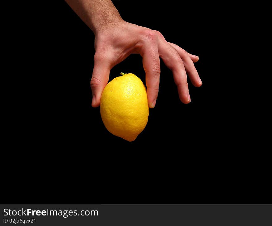 Male hand holding a yellow lemon. On a black background.