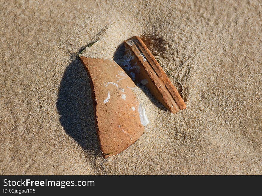 Close view of a broken ceramic pot buried on the sand. Close view of a broken ceramic pot buried on the sand.