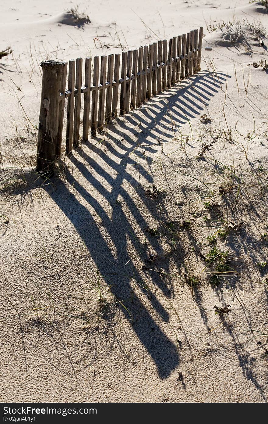 View of a section of a fence buried on the dune sand on the beach. View of a section of a fence buried on the dune sand on the beach.