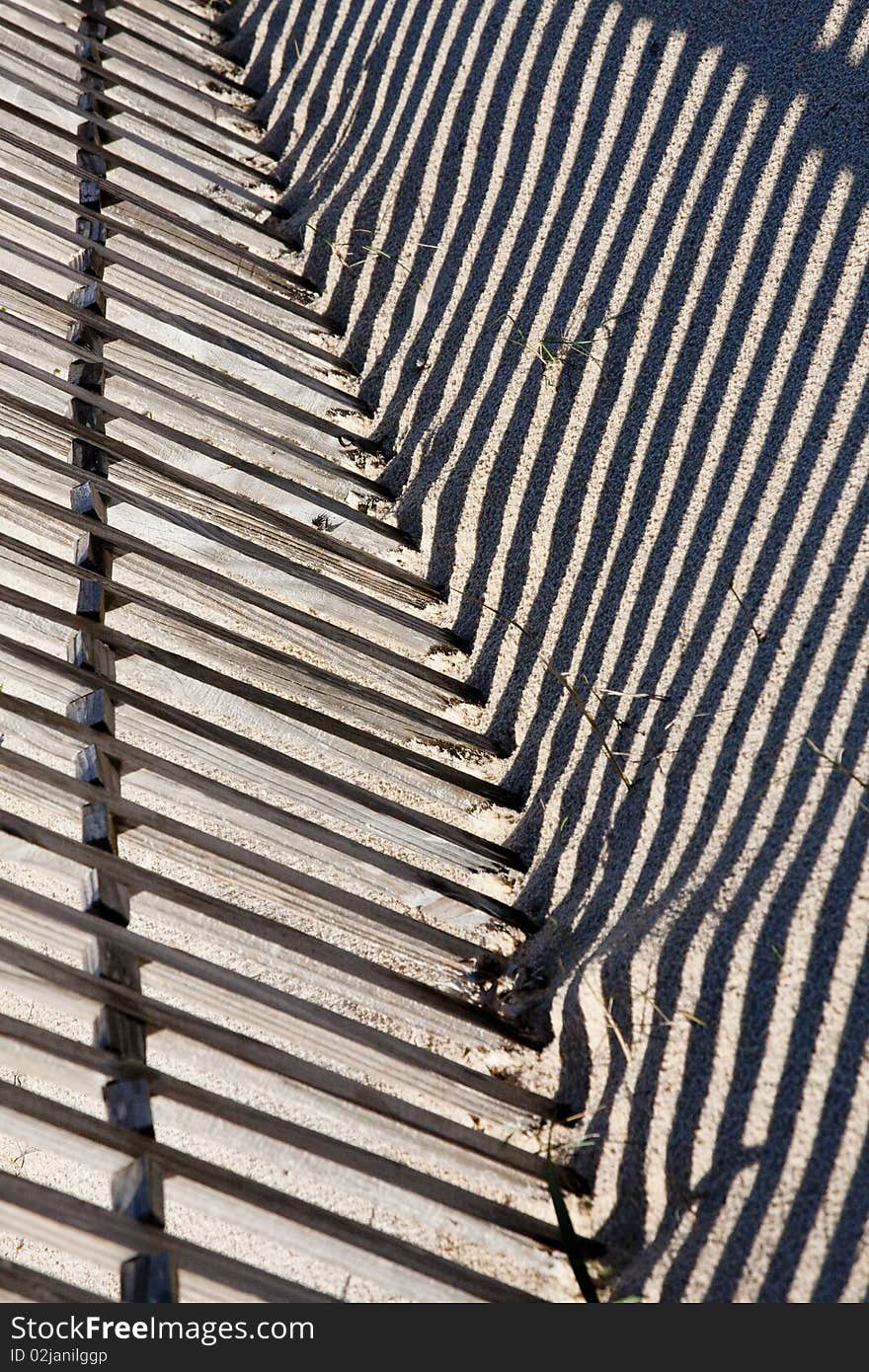 View of a section of a fence buried on the sand making a shadow. View of a section of a fence buried on the sand making a shadow.