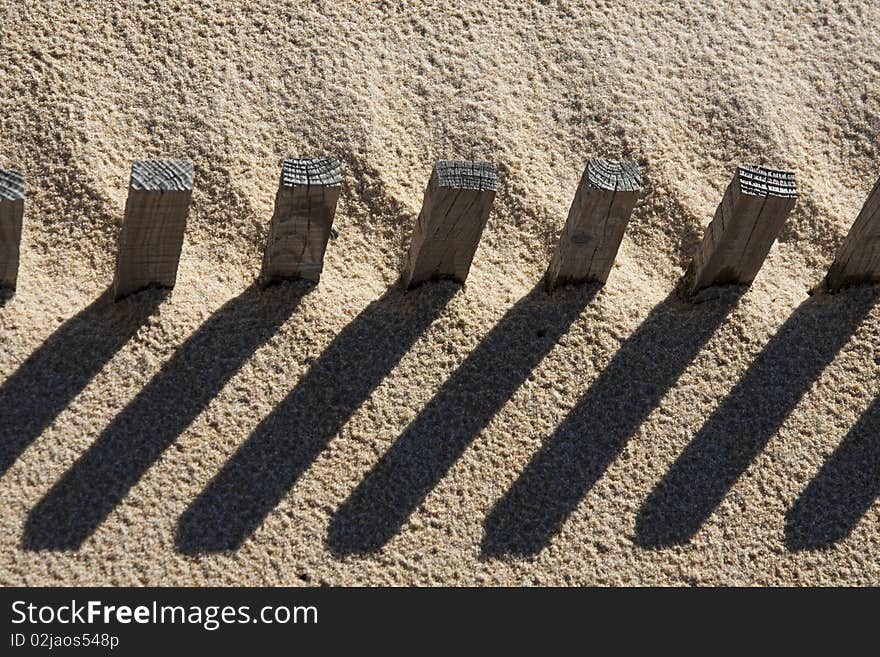 View of a section of a fence buried on the sand making a shadow. View of a section of a fence buried on the sand making a shadow.