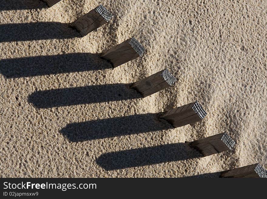 View of a section of a fence buried on the sand making a shadow. View of a section of a fence buried on the sand making a shadow.