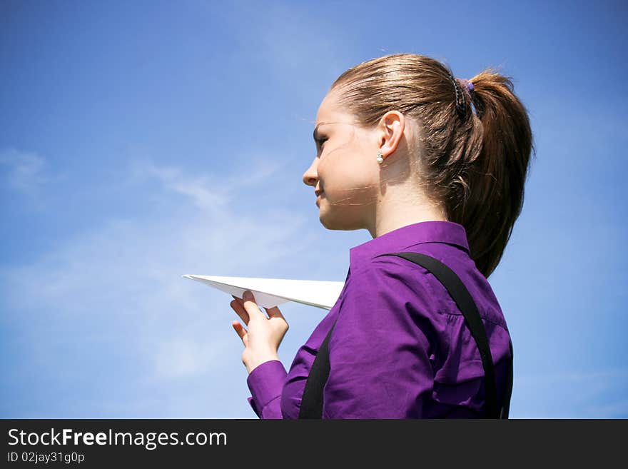 Young businesswoman with paper plane in the hand against blue sky