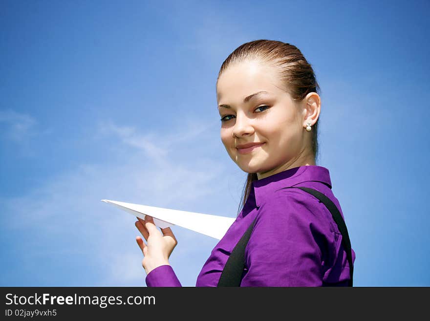 Young caucasian girl with paper plane in the hand against blue sky