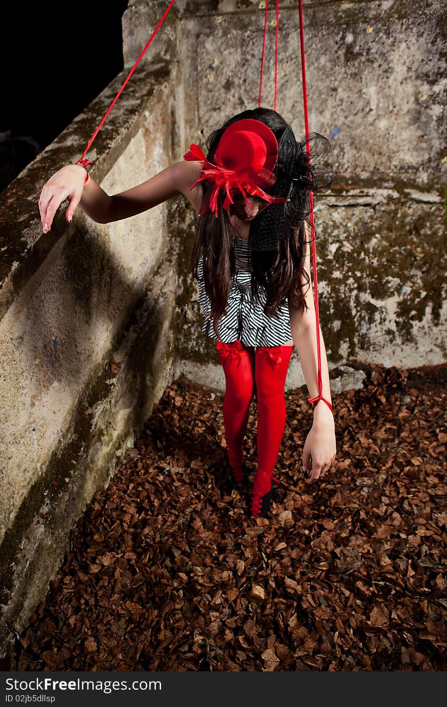 Beautiful girl wearing red hat and striped dress posing as a marionette (puppet on a string)