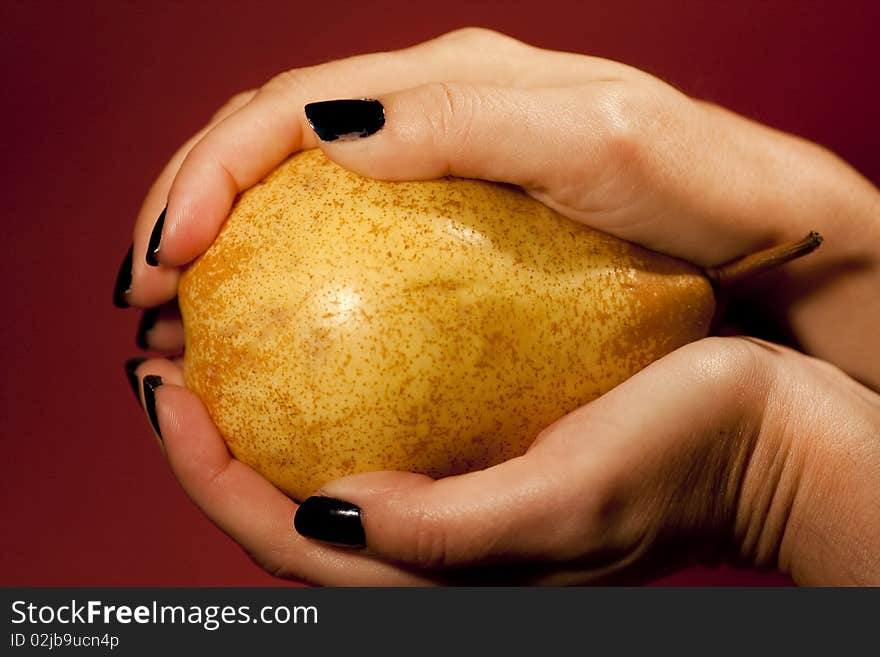 Close view of a woman hands holding a pear over a red background.